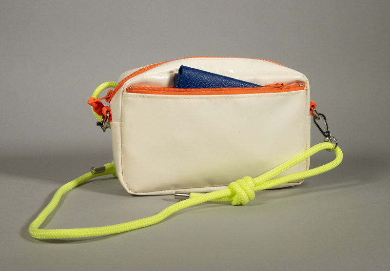 Sac zippé en bâche blanche upcyclée, compartiment principal zippé et poche avant zippée, zip orange fluo, sangle détachable en paracord jaune fluo avec mousquetons — présenté ouvert avec un porte-monnaie en cuir bleu glissé à l'intérieur.