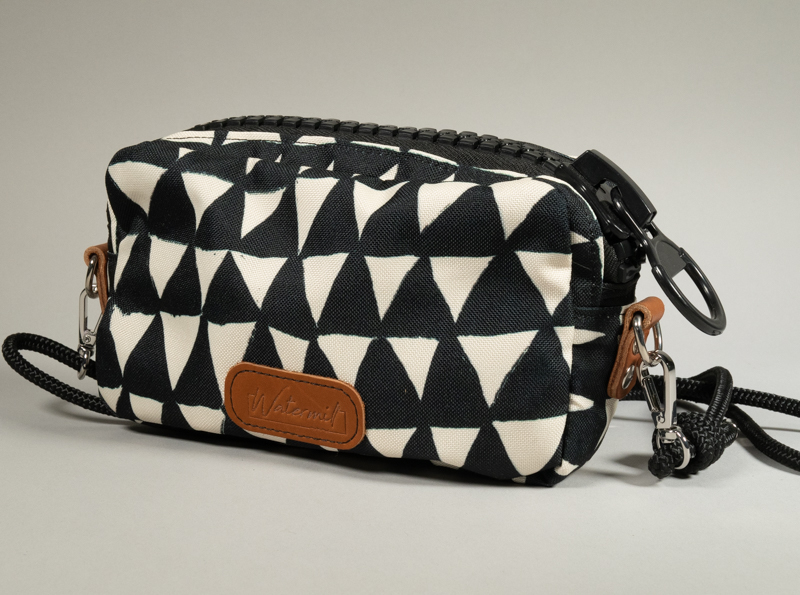 Sac zippé Watermill × Pures Folies en toile imperméable motif triangles noir et blanc, vue de dos avec étiquette cuir camel Watermill en façade, zip XXL noir mat, départs d'anneaux en cuir camel, sangle paracord noir détachable avec mousquetons.
