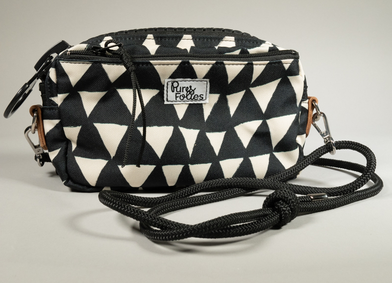 Sac zippé Watermill × Pures Folies en toile imperméable motif triangles noir et blanc, zip XXL noir mat, départs d'anneaux en cuir camel, sangle paracord noir détachable avec mousquetons, étiquette Pures Folies en façade