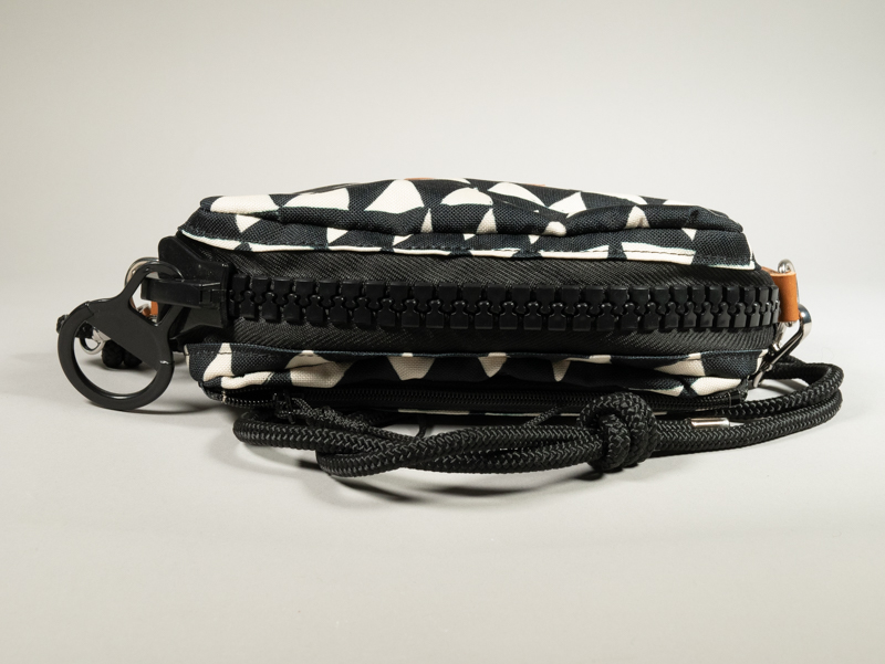 Sac zippé Watermill × Pures Folies en toile imperméable motif triangles noir et blanc, vue de dessus montrant le zip XXL noir mat, les départs d'anneaux en cuir camel contrasté et la sangle paracord noir avec mousquetons.