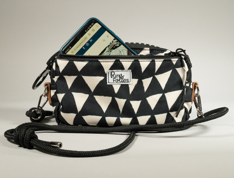 Sac zippé Watermill × Pures Folies en toile imperméable motif triangles noir et blanc, présenté ouvert avec un smartphone glissé dans le compartiment principal, zip XXL noir mat, départs d'anneaux en cuir camel et sangle paracord noir détachable.