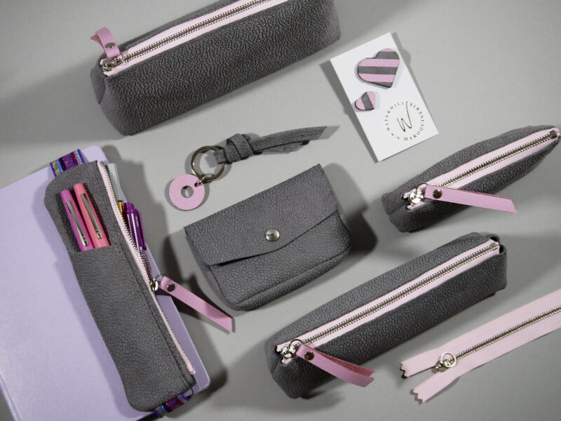 trousse élastique en croûte de cuir grainé gris clair, zip contrasté rose pastel , compartiment avant pour accès rapide , élastique arc en ciel, présenté avec accessoires coordonnés: pin's, porte clés, trousse berlingot