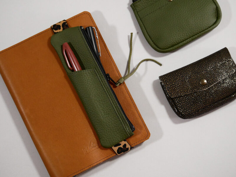 trousse élastique en cuir grainé kaki avec compartiment avant pour accès rapide , élastique léopard noir et camel, présenté sur protège agenda en cuir camel et accessoires coordonnés: porte-monnaie zippé et clutch
