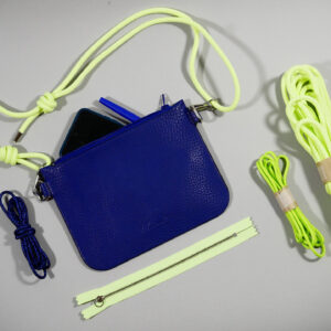 la Nomade: pochette en cuir grainé bleu roi avec sangle en paracord jaune fluo ajustable grâce à des noeuds présentée avec des Paracord et un zip fluo