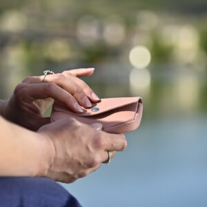 porte monnaie clutch en cuir grainé rose poudré dans les mains d'un mannequin au bord de l'eau collection intemporels
