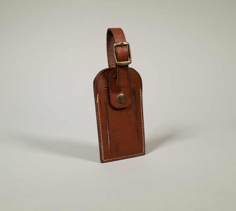 Porte étiquette de bagage en cuir lisse havane avec fermeture par pression et boucle en laiton vieilli.