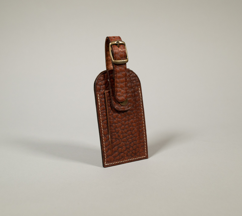 Porte étiquette de bagage en cuir havane grainé avec fermeture par pression et boucle en laiton vieilli.