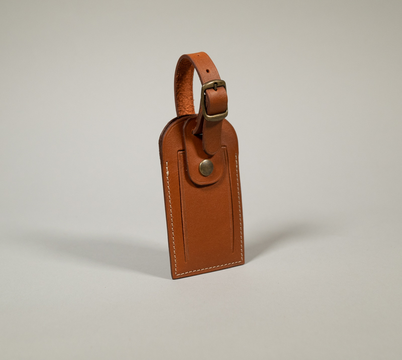 Porte étiquette de bagage en cuir camel avec fermeture par pression et boucle en laiton vieilli.
