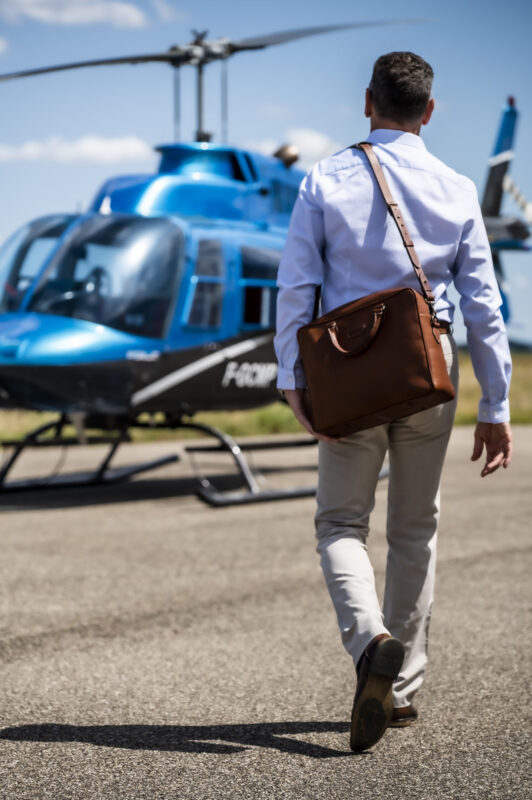 sac ordinateur, business, 24h en cuir de couleur havane, porté par un mannequin marchant vers un hélicoptère
