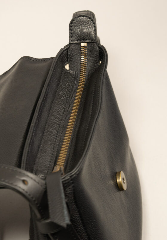 détails du zip sous rabat de la besace mini INTEMPORELS, en cuir noir grainé et cuir contrasté noir lisse