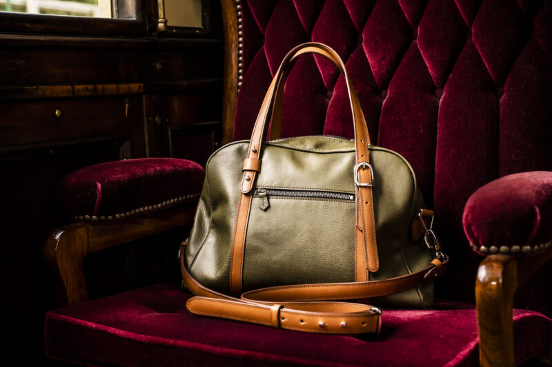 sac bowling bronze et camel posé sur siège matelassé de wagon en velours rouge
