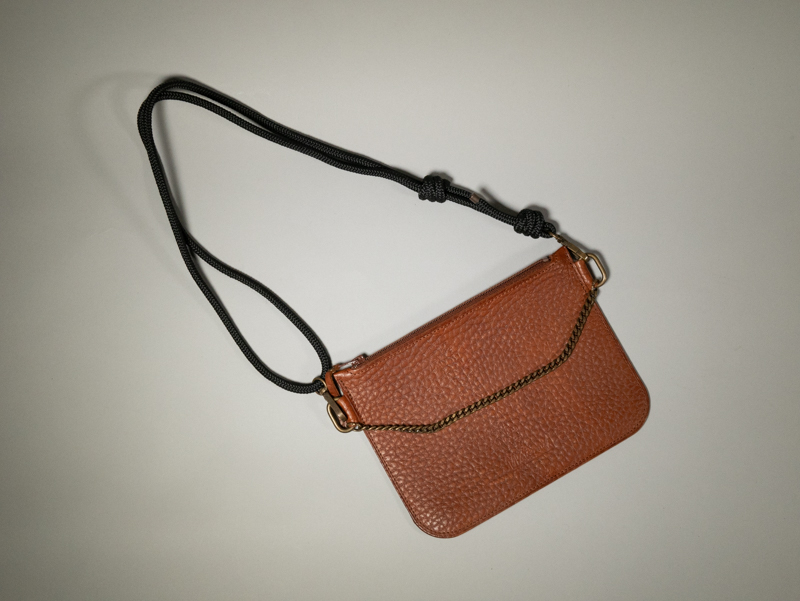 la Nomade: pochette en cuir grainé havane avec sangle en paracord noire ajustable grâce à des noeuds, ornée d'une chainette métal laiton vieilli