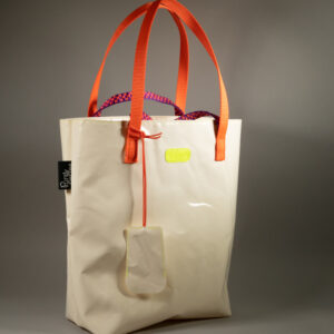 Tote bag en bâche blanche upcyclée, double anse — sangle plate orange fluo et corde paracord violet et orange tressé — logo Watermill jaune fluo, avec porte-clés cloche en bâche attaché par une cordelette paracord orange. Étiquette Pures Folies visible sur le côté.