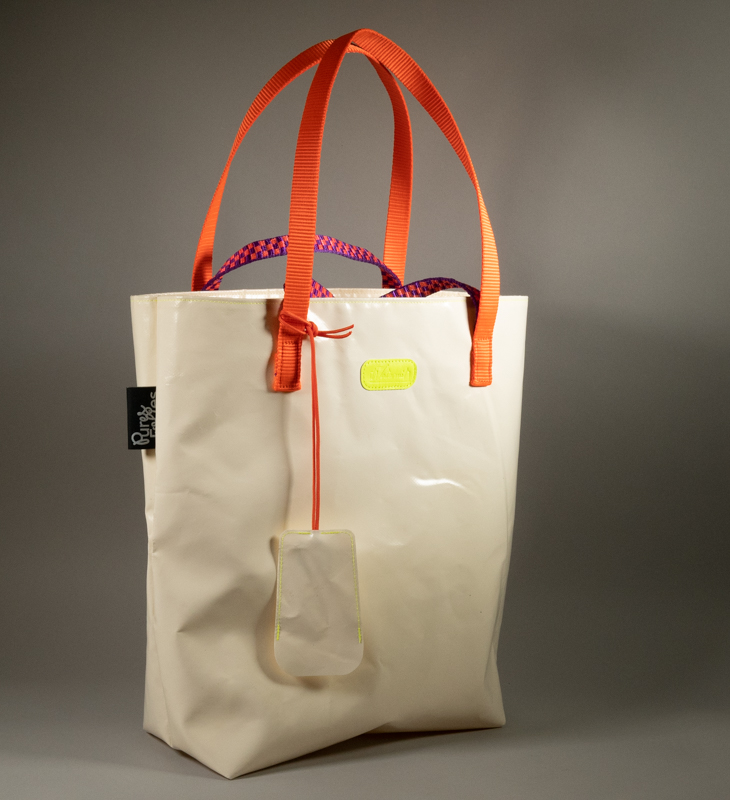 Tote bag en bâche blanche upcyclée, double anse — sangle plate orange fluo et corde paracord violet et orange tressé — logo Watermill jaune fluo, avec porte-clés cloche en bâche attaché par une cordelette paracord orange. Étiquette Pures Folies visible sur le côté.