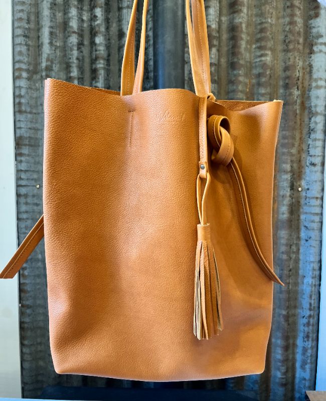 Tote bag Watermill en cuir souple camel avec pochette intérieure amovible et pompon en cuir, présenté devant une tole d'atelier