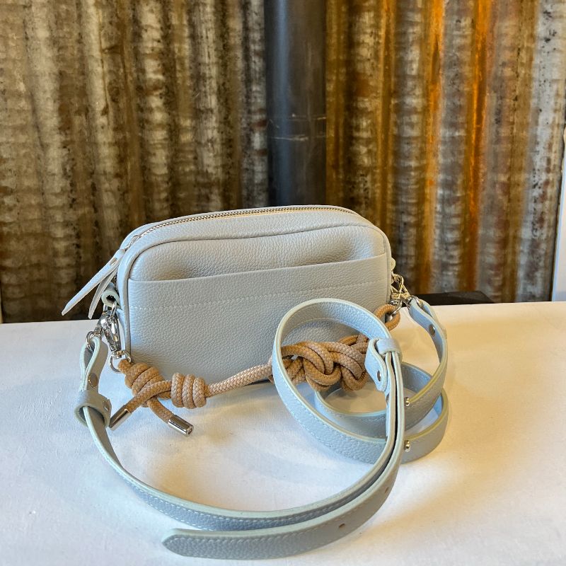 Sac à main camera case, en cuir avec poche avant, de couleur gris bleu glacier, avec bandoulières cuir et corde et posé devant une tôle d'atelier